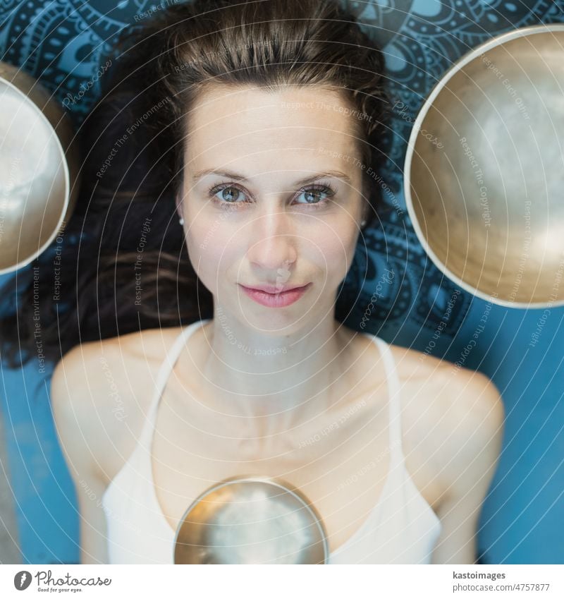 Yoga concept, meditation and sound therapy. Portrait of beautiful young caucasian woman surrounded by copper tibetan singing bowls and instruments buddhism