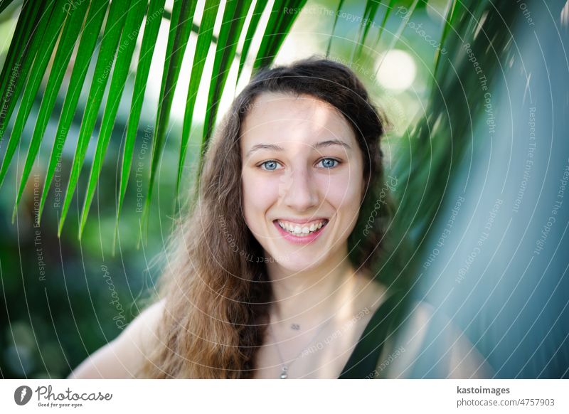 Young beautiful natural cheerful woman with healthy face and skin in exotic greenery. Closeup fresh face of attractive girl. Summer model. Natural beauty concept.