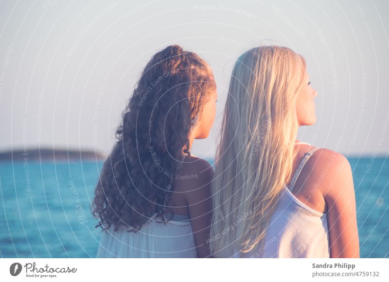 Blondegirl with straight hair and dark haired girl with curly hair from behind smooth Curly dark blond Hair and hairstyles Woman View into the distance Sunset