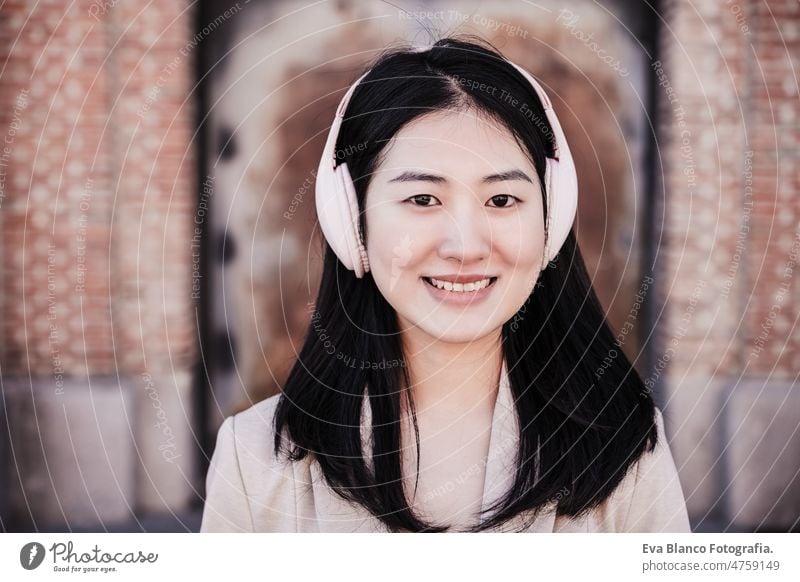 close up of smiling woman listening to music on headphones and mobile phone in city happy chinese head phones crossing street urban lifestyle daytime asian