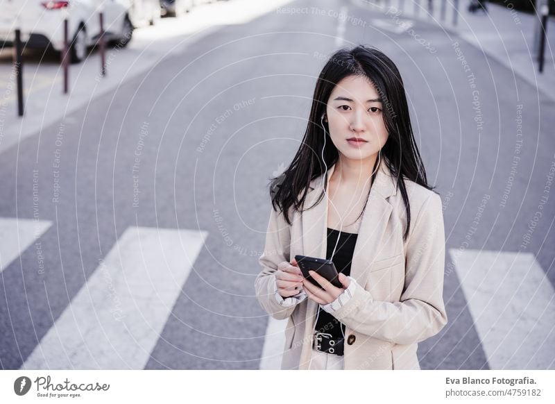 confident business woman listening to music on headphones and mobile phone crossing street in city chinese head phones happy smiling urban lifestyle daytime