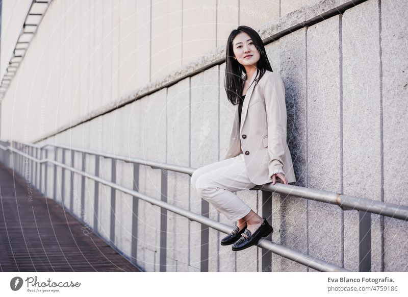 confident beautiful chinese business woman sitting on railing in city asian laptop technology cafe coffee cafeteria tablet mobile phone cheerful young desk