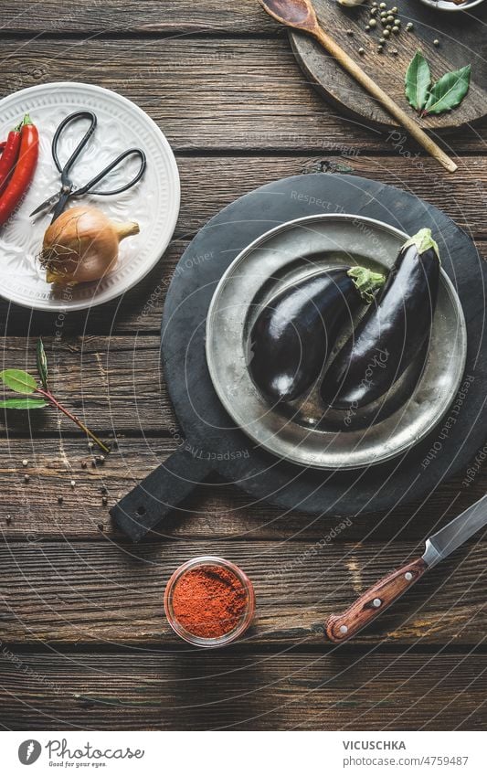 Food background with eggplant on plate and cutting board with herbs. Healthy ingredients food background healthy kitchen utensils rustic wooden table cooking