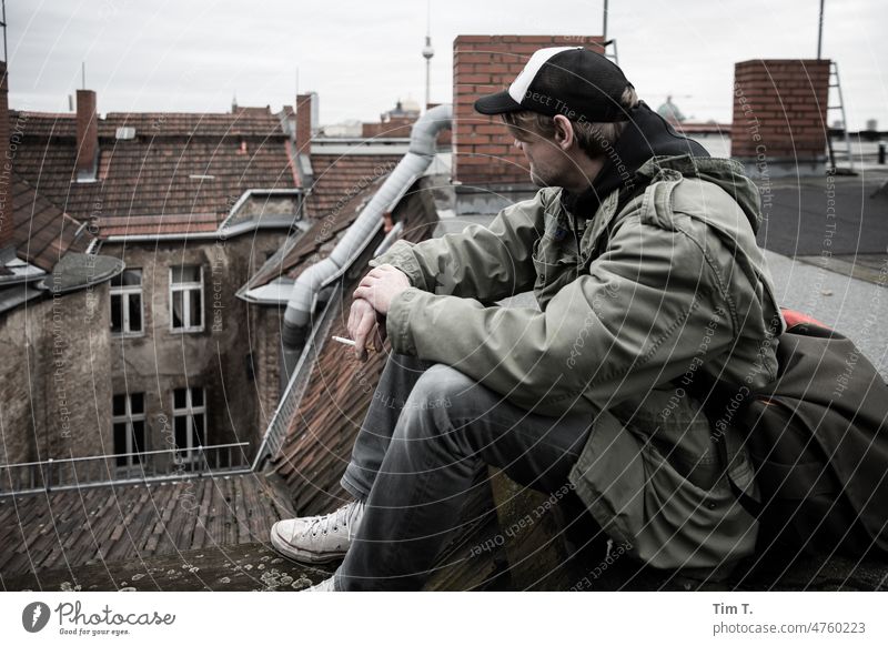 a man with baseball cap and cigarette sits on a roof. In the background you can see the TV tower. Berlin Downtown Berlin Berlin TV Tower Middle Roof Man