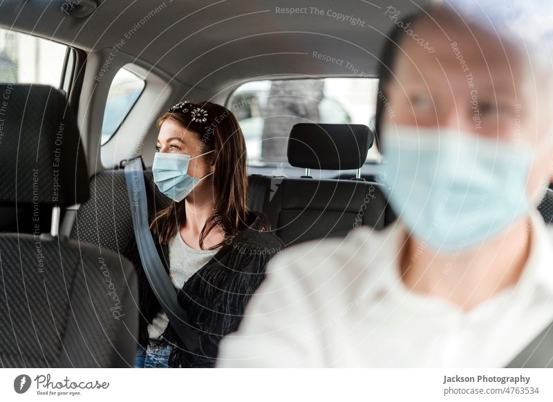 A woman wearing a protective mask on the back seat of a taxi car tourist passenger driver uber client reflection private smile happy discover traveler commuter