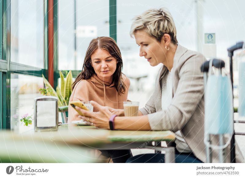 Two female travelling friends enjoying time in cafe - mask and luggage in the foreground women wait phone transportation adult attractive bag beverage blonde