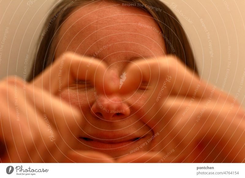 A woman forms a heart with her fingers in front of her face and shows a laughing mouth Heart shape Fingers symbolic In love Laughter fortunate gesture Woman