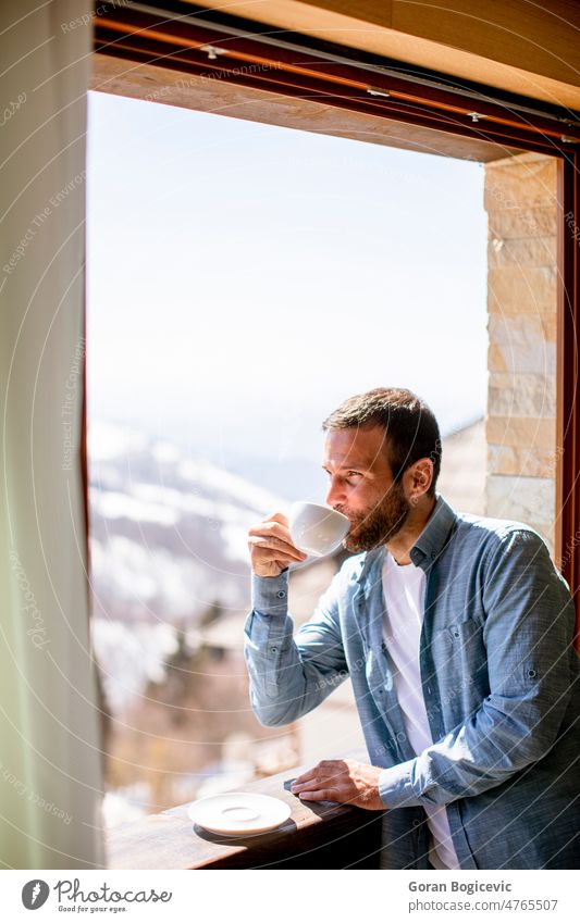 Young man with cup of hot tea at winter window apartment attractive beautiful beverage calm coffee cute drink enjoying face home hotel house interior indoors