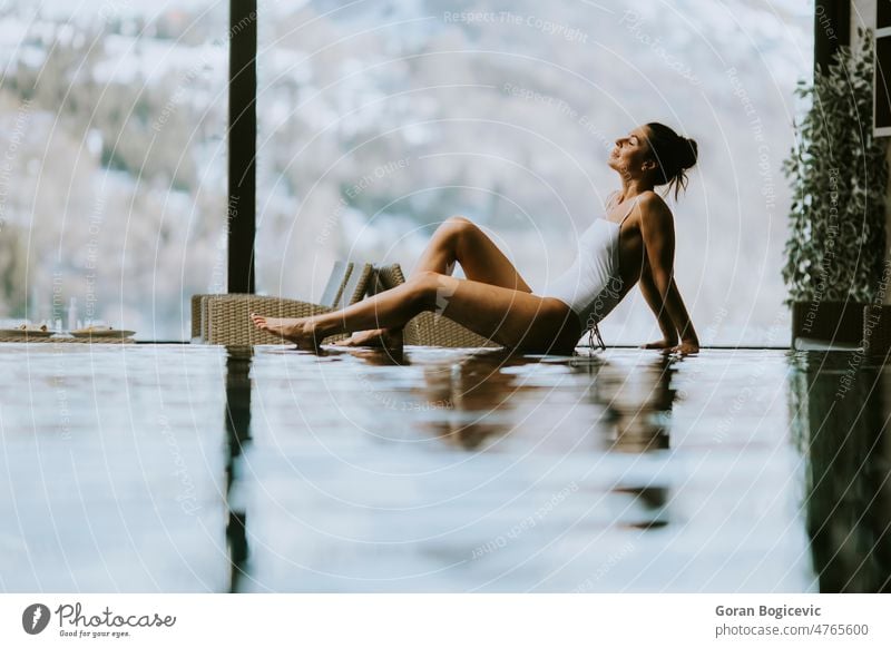 Young woman relaxing on the poolside of infinity swimming pool at winter time 20s adult attractive beauty bikini body brunette caucasian enjoy enjoyment female