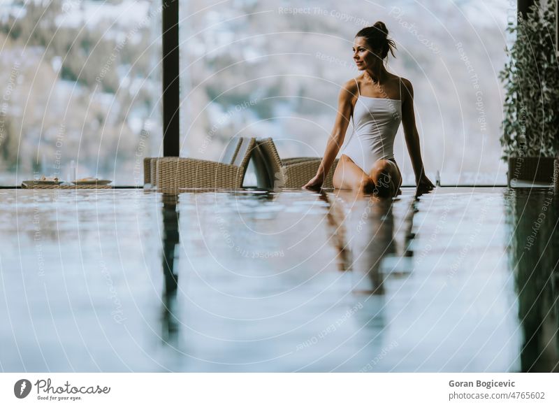 Attractive young woman in bikini sits by the poolside in the indoor swimming pool winter spa relax relaxation beautiful wellness female resort lifestyle warm