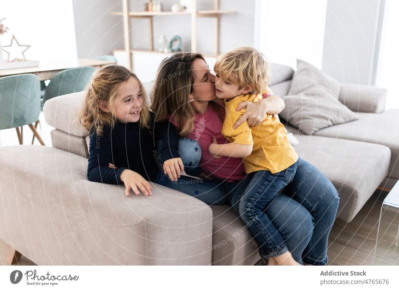 Mother kissing son near daughter mother children sibling pastime spend time living room love childhood caress motherhood bonding together childcare sofa boy