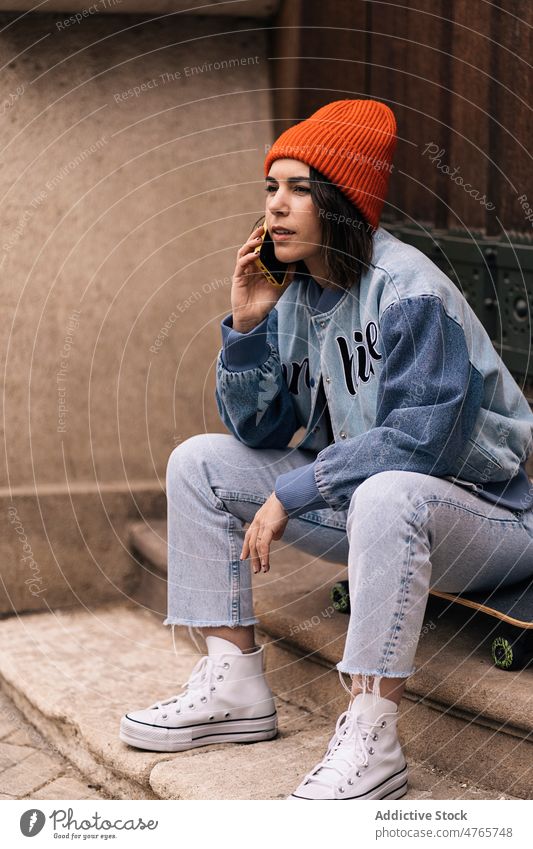 Woman talking on smartphone near building woman phone call conversation skateboard street street style city urban hobby appearance female town lady garment