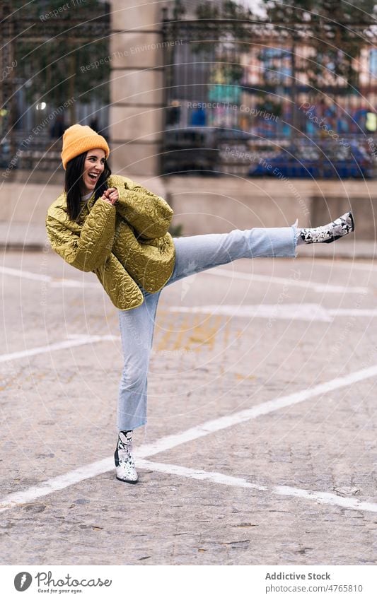 Woman doing leg kick on street woman city urban appearance practice skill perform energy female cheerful glad headwear positive smile sidewalk content cloth