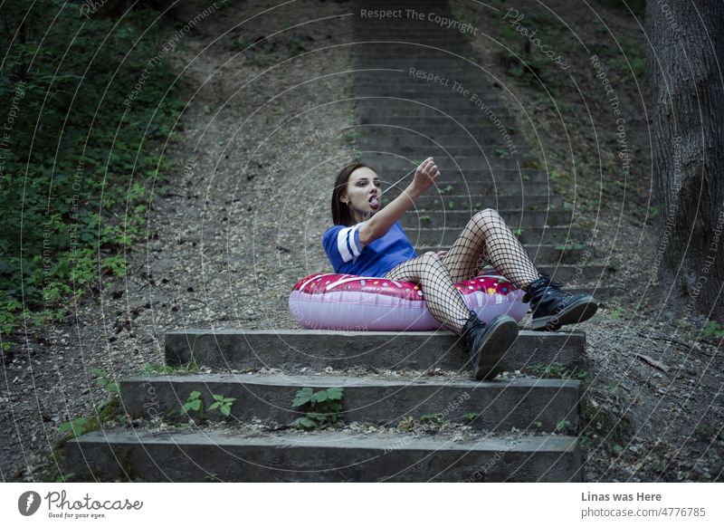 A gorgeous brunette girl is having some fun in the woods. Her pretty long legs are in fishnets. Chewing bubble gum. Sitting on a swimming wheel. And having some fun in general.