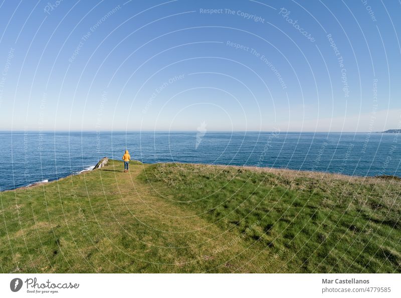 Coastal landscape and girl in yellow hooded coat looking at sea and walking. Copy space. coast sky coastline woman person jacket sightseeing tourism travel