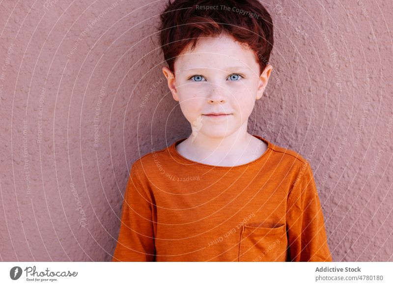 Cute boy standing near wall red hair kid street appearance childhood style casual candid gaze cute portrait adorable city smile content summertime light color