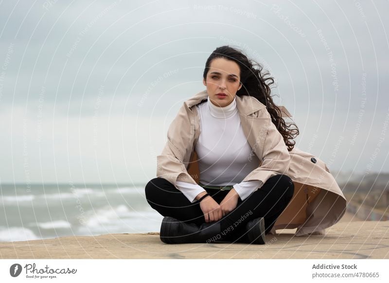 Charming woman on beach on windy day coast water sea seaside wave coastal dreamy feminine flying hair seashore weather lady nature attractive female sand coat