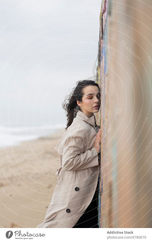 Peaceful woman near wall on shore coast beach water sea seaside coastal feminine dreamy flying hair seashore weather lady nature attractive female sand coat