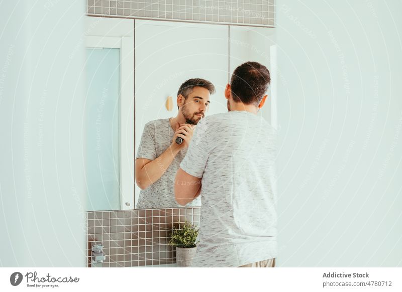 Man shaving beard with trimmer man shave routine unshaven mirror hygiene daily bathroom reflection home appearance male light guy everyday procedure treat