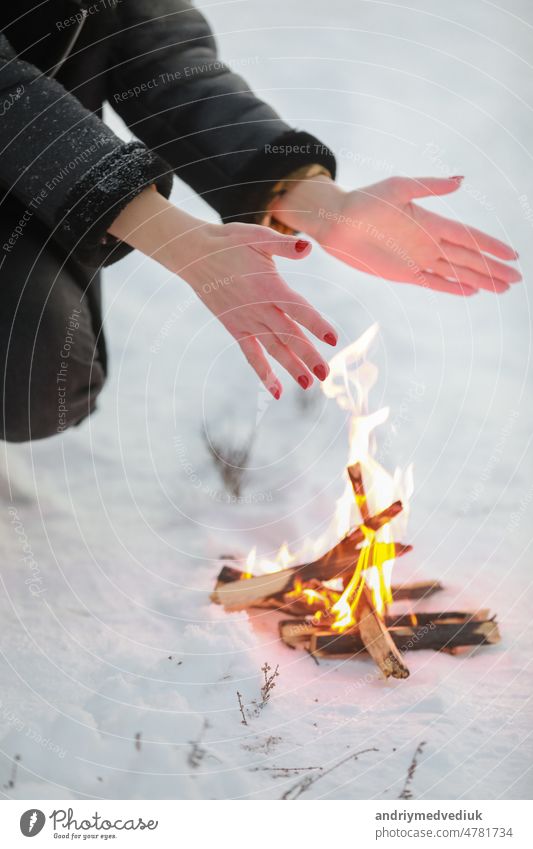 cropped photo of young woman warms her hands over bonfire in winter forest. Close-up outdoor snow cold nature travel female picnic girl happy lifestyle wood