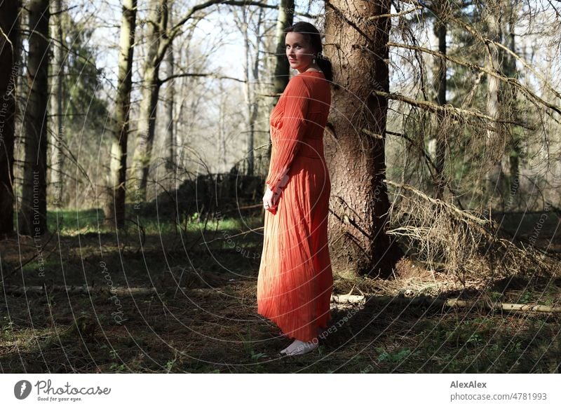 Young woman in red dress stands in spring forest and poses for camera Woman youthful pretty Long-haired Brunette daintily Beauty & Beauty 18 - 30 years