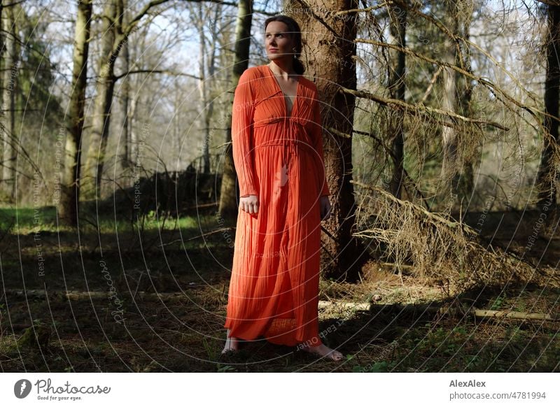 Young woman in red dress stands in spring forest and poses for camera Woman youthful pretty Long-haired Brunette daintily Beauty & Beauty 18 - 30 years