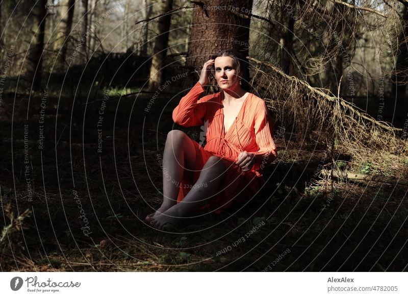 Young woman in red dress sits in spring forest and looks at camera Woman youthful pretty Long-haired Brunette daintily Beauty & Beauty 18 - 30 years