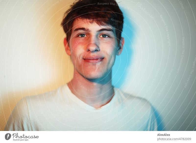 Portrait of young man with dimples in cheeks in yellow and blue light in front of white wall Boy (child) Man Young man younger Large pretty Strong Athletic