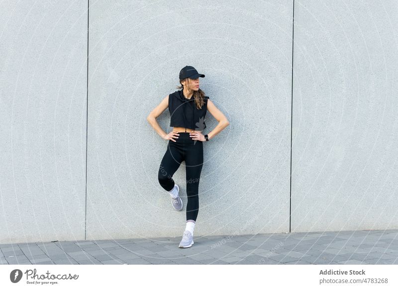 Sportswoman standing near wall and having break on street sportswoman city athlete training workout rest activewear sporty lean healthy lifestyle wellbeing cap