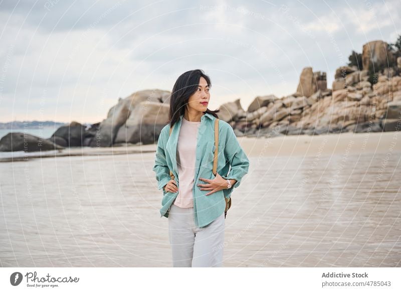 Beautiful Asian girl walking on the beach in Autumn during her trip nature rocks cloudy sand wet wet sand Chinese girl woman one person people portrait winter