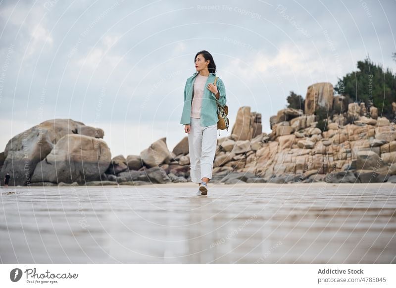 Beautiful Asian girl walking on the beach in Autumn during her trip nature rocks cloudy sand wet wet sand Chinese girl woman one person people portrait winter