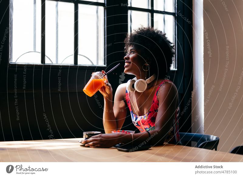 Cheerful woman drinking fruit juice in cafe breakfast headphones happy cheerful joyful female fresh diet vitamin meal young food natural orange morning