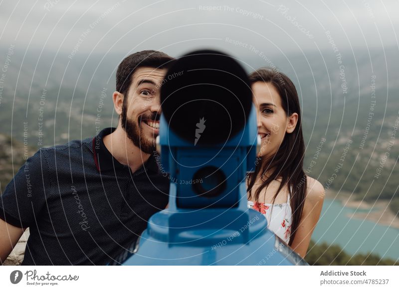 Cheerful couple having fun with binocular on town observation deck mountain cheerful playful playing joyful explore casual viewpoint countryside valley foggy