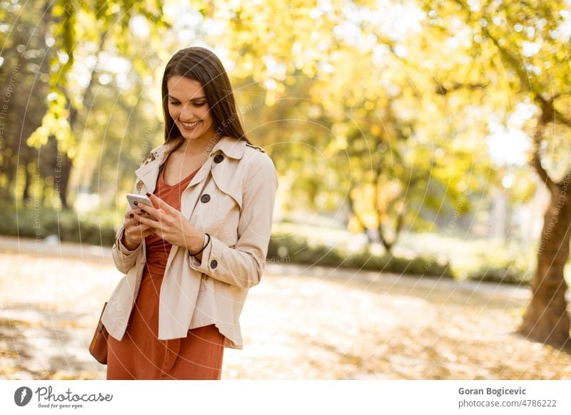 Happy young woman using cell phone in autumn park female person fall beautiful adult communication telephone portrait beauty season smiling mobile outdoor