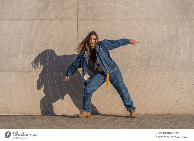 Young woman standing making movements with her body while looking at camera young arms front view sunlight wall outside one person female lifestyle fashion