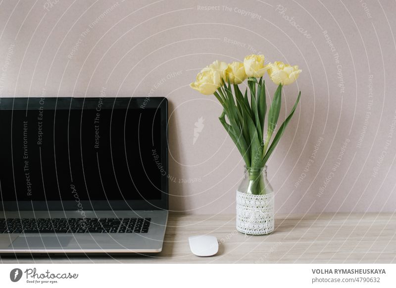 Spring home office still life composition. Blank laptop screen. Yellow tulips in a vase on the table. Office workplace. Scandinavian interior. desk display