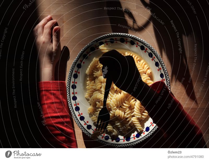 Plate with fusilli, child's hand left in sunlight, right arm in shade, just about to stick fork into fusilli Noodles Eating steam Hot Lunch Interior shot