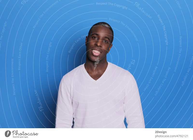 Smiling young african american man guy in casual white sweater posing isolated on pastel blue background studio portrait. black male smile positive cheerful