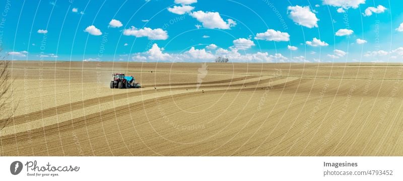 Arable farming. Farmer with tractor sowing grain on field. blue tractor with harrow on field against cloudy sky, farm machinery work. Land preparing for sowing