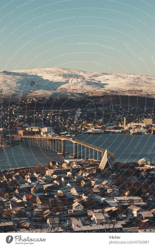 View of the polar town of Tromso in northern Norway and the snowy hills in the background at sunset. The landmark of this Paris of the North - Tromso bridge in Finnmark county, Norway