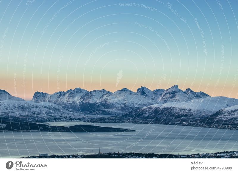 view of the polar town of Tromso in northern Norway and the snowy hills in background at sunset. Orange-red colour lines rocky mountains. Exploring the world. A Scandinavian city and beauty of nature