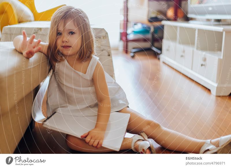 Sad little girl with a drawing book sitting on the floor in the living room sad child person childhood kid emotion alone sadness caucasian upset female indoor