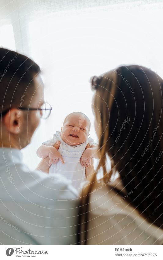 Mother and father from behind holding their newborn son gesturing. New parents gesture mother new parents parenthood motherhood wife husband indoor mom together