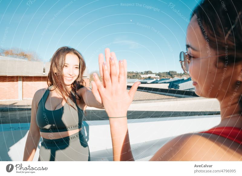 Two young woman celebrate finishing a outdoor exercise session. Happy friends training together during a sunny summer day preparing for the beach body person