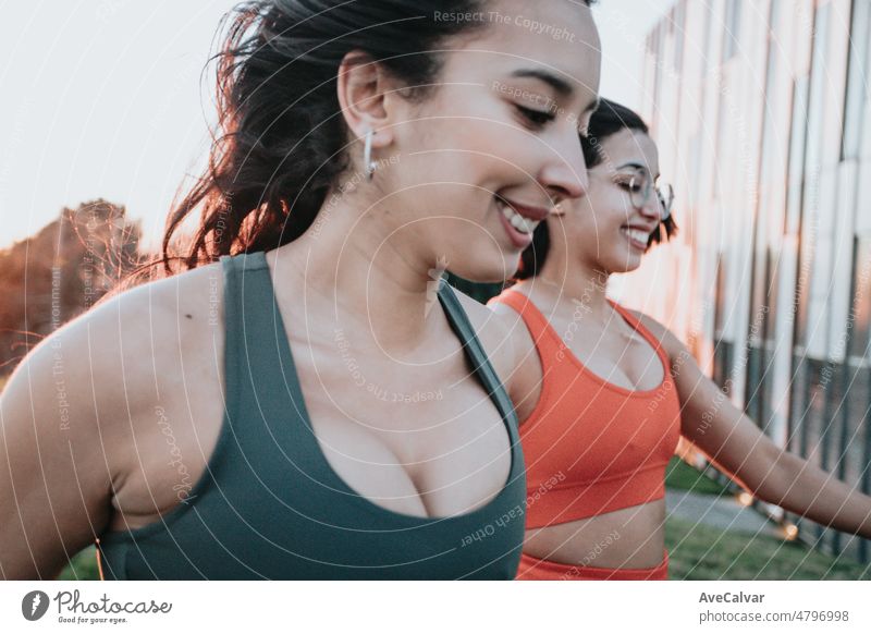 Two young woman running together during a outdoor exercise session. Happy friends training together during a sunny summer day preparing for the beach body