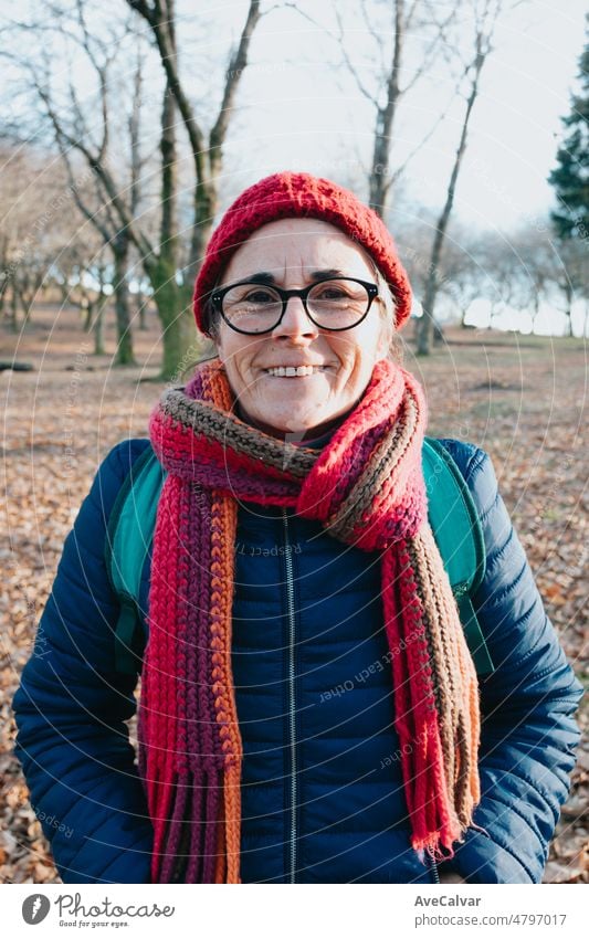 Frontal portrait of an old woman smiling to camera using glasses and a cap for the cold and winter.. Aging well and healthy concept, family grandmother image. Active third age concept