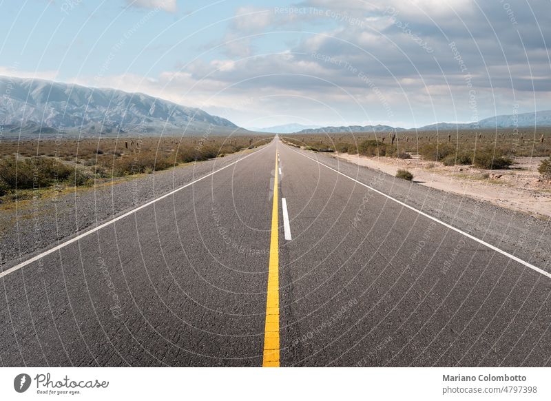 A long empty road surrounded by hills and mountains during a partially cloudy day road trip Vanishing point travel lines nature arid journey asphalt landscape