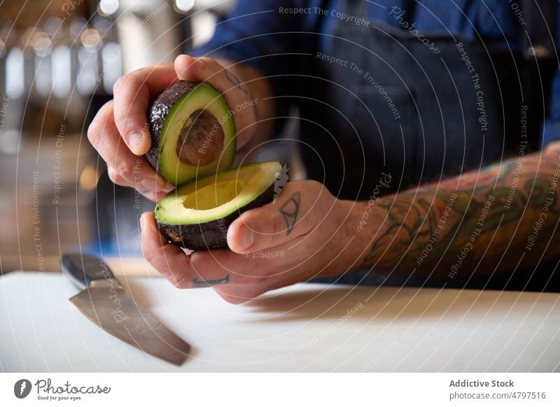 Anonymous concentrated chef cutting ripe avocado man vegetable kitchen cook culinary cuisine ingredient product food prepare cutting board male fresh tattoo