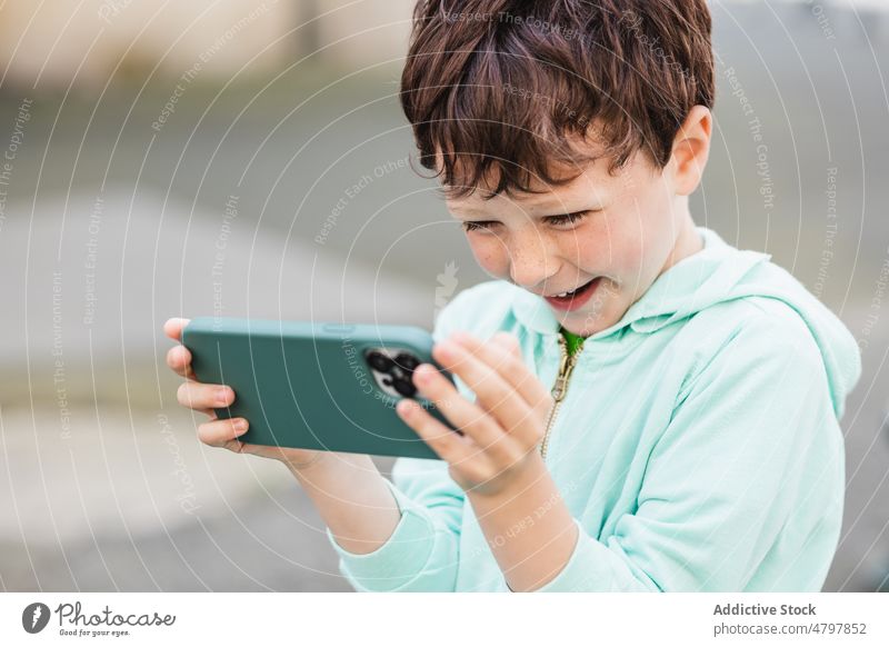 Happy boy using smartphone near blue wall happy watch video smile street online kid mobile internet cheerful glad connection content delight child little device