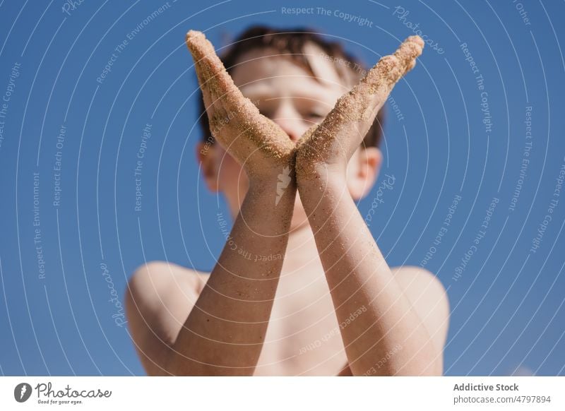 Boy showing hands covered with sand boy kid summer coast childhood rest recreation messy pastime leisure tropical blue sky naked torso shirtless cute cloudless